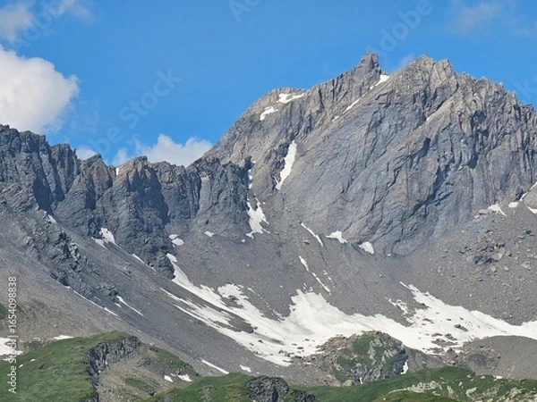 Fototapeta La Thuile, Val D'Aosta, July 02 2025: Panoramic view to the alps, beautiful green landscape reflected in a small natural lake. Beautiful blue sky with some clouds. Mountains with a little snow. Aerial