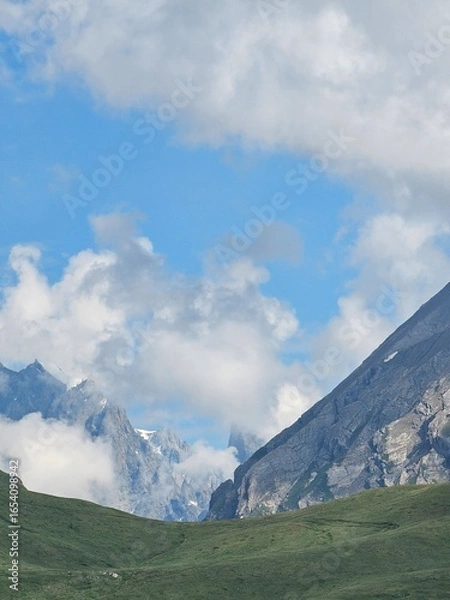 Fototapeta La Thuile, Val D'Aosta, July 02 2025: Panoramic view to the alps, beautiful green landscape reflected in a small natural lake. Beautiful blue sky with some clouds. Mountains with a little snow. Aerial