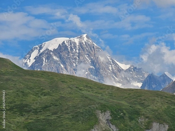 Fototapeta La Thuile, Val D'Aosta, July 02 2025: Panoramic view to the alps, beautiful green landscape reflected in a small natural lake. Beautiful blue sky with some clouds. Mountains with a little snow. Aerial
