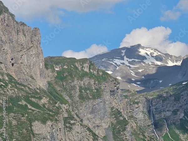 Fototapeta La Thuile, Val D'Aosta, July 02 2025: Panoramic view to the alps, beautiful green landscape reflected in a small natural lake. Beautiful blue sky with some clouds. Mountains with a little snow. Aerial