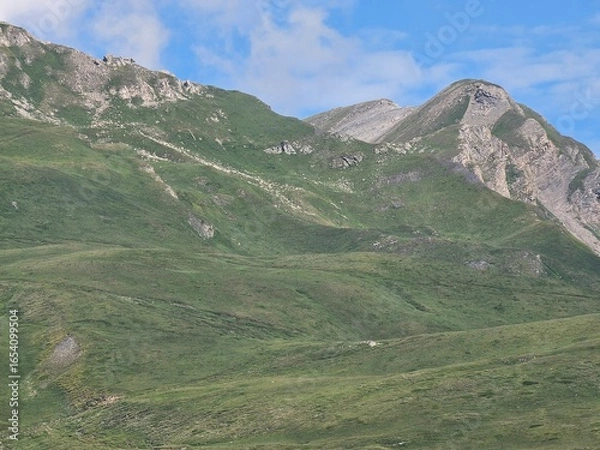 Fototapeta La Thuile, Val D'Aosta, July 02 2025: Panoramic view to the alps, beautiful green landscape reflected in a small natural lake. Beautiful blue sky with some clouds. Mountains with a little snow. Aerial