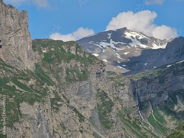 Fototapeta La Thuile, Val D'Aosta, July 02 2025: Panoramic view to the alps, beautiful green landscape reflected in a small natural lake. Beautiful blue sky with some clouds. Mountains with a little snow. Aerial