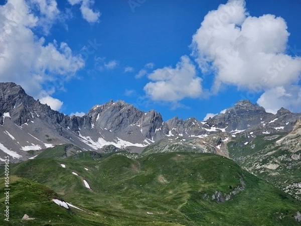 Fototapeta La Thuile, Val D'Aosta, July 02 2025: Panoramic view to the alps, beautiful green landscape reflected in a small natural lake. Beautiful blue sky with some clouds. Mountains with a little snow. Aerial