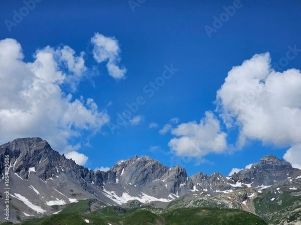 Fototapeta La Thuile, Val D'Aosta, July 02 2025: Panoramic view to the alps, beautiful green landscape reflected in a small natural lake. Beautiful blue sky with some clouds. Mountains with a little snow. Aerial