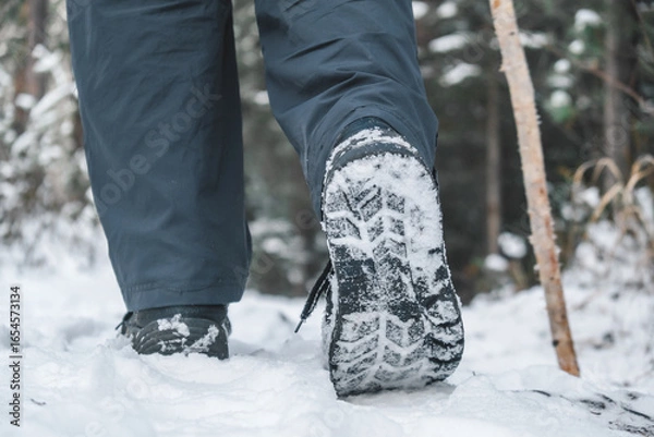 Fototapeta boots leave clear footprints in snow as traveler hikes through serene forest trail in winter. trees surround path, creating peaceful atmosphere. close up.