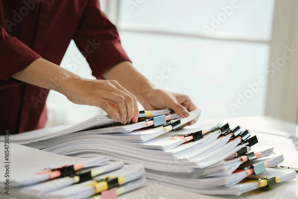 Fototapeta A cluttered office desk filled with paperwork, documents, files, and reports, symbolizing heavy workload, financial management, research, business tasks, corporate responsibilities, stress, and organi