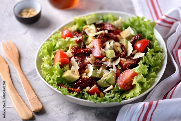 Fototapeta Salad from lettuce, cherry tomatoes, dried tomatoes, avocado, parmesan, pine nuts with olive oil. Healthy food.