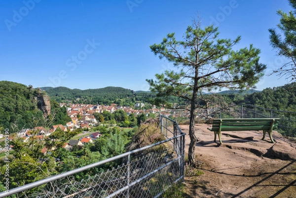 Obraz  A green wooden bench on a high viewpoint overlooking the town of Dahn, with the town's buildings and the forested hills of the Pfälzerwald visible in the valley below.