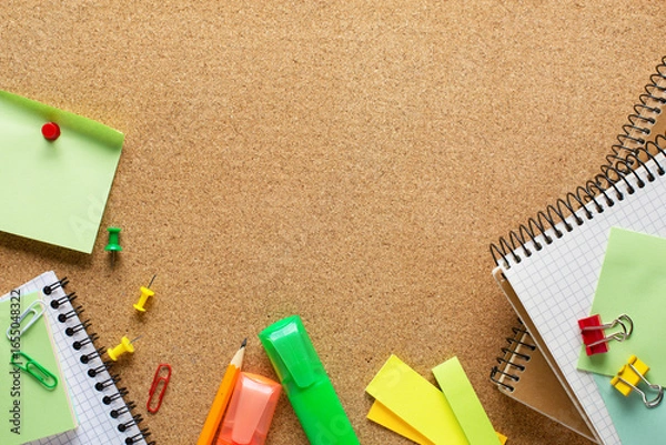 Fototapeta Notepads, markers, pencil, sticky notes, paper sheets, paper clips and binder clips  on cork board  with copy space for text.  Top view of colorful school supplies.