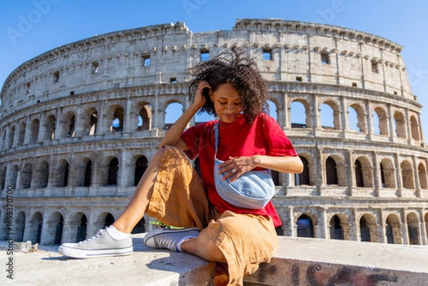 Fototapeta A woman is enjoying a quiet and reflective moment at the iconic Colosseum in Rome, where ancient history beautifully blends with her modern stylish attire, creating a memorable experience