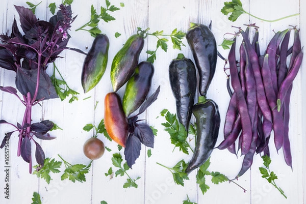 Fototapeta Purple vegetables harvested from a summer garden. Peppers, tomatoes, beans, and basil against a white wood background. Medicinal properties of anthocyanin