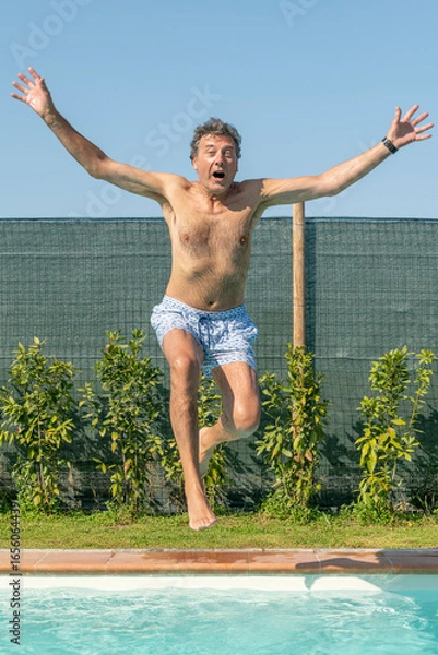 Fototapeta A man jumps with his arms outstretched to dive into the pool
