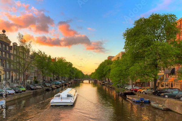 Fototapeta Tourist Canal tour boat at sunset in one of the beautiful canals of Amsterdam, The Netherlands