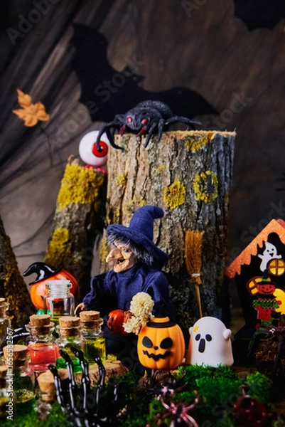 Fototapeta halloween, mysterious forest, witch on Polyanka sits on a stump in her cozy shelter with spiders, a ghost, an eye, pumpkins and conjures over jars of potions on the eve of All Saints Day