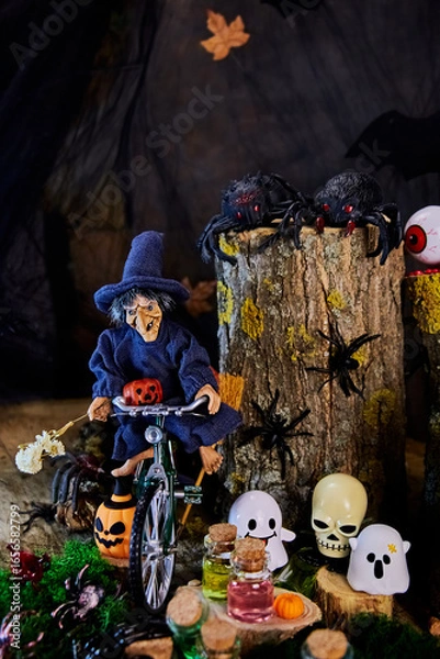 Fototapeta witch rides a bike to celebrate All Saints Day in a creepy cobweb forest with spiders, ghosts, skull and other Halloween characters, vertical, creative focus