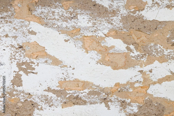 Fototapeta Old weathered wall surface with peeling white paint and exposed rough plaster texture. Rustic grunge background with cracked paint, chipped plaster, and distressed vintage look