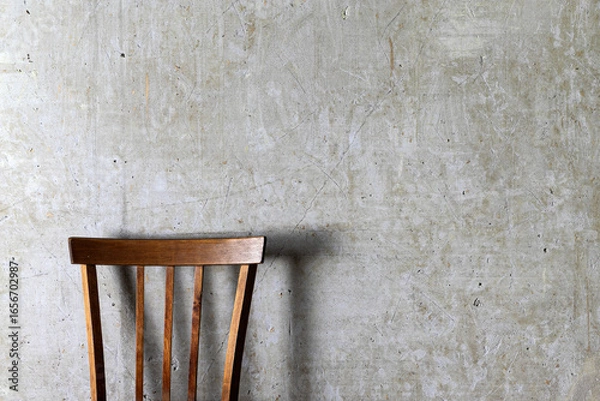 Fototapeta A minimalistic photo of a wooden chair with vertical slats placed against a textured concrete wall.