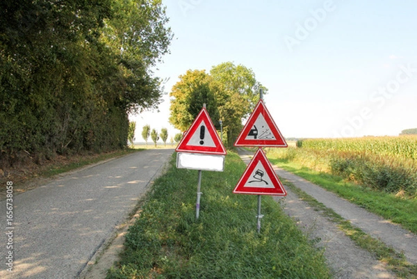 Fototapeta traffic signs for risk of slipping and flying stones in the verge of a country road with new asphalt