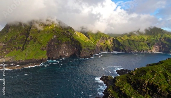 Fototapeta Rugged coastal landscape showcases dramatic cliffs, lush greenery, and a tranquil body of water, bathed in the soft light of a partly cloudy day.