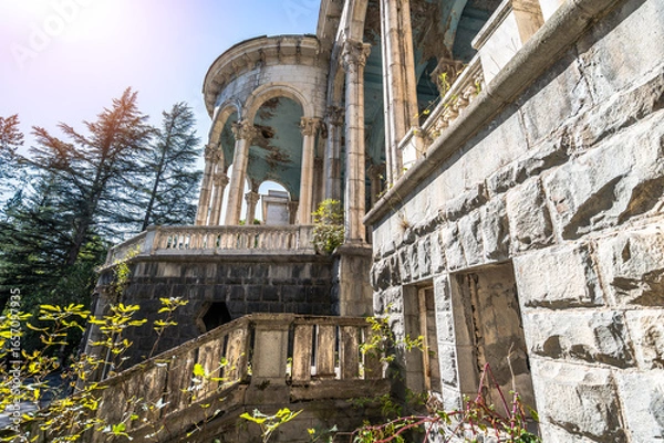 Fototapeta Abandoned neoclassical building in Georgia with cracked walls, ruined columns, decaying stone structure, overgrown plants, soviet architecture, derelict landmark.