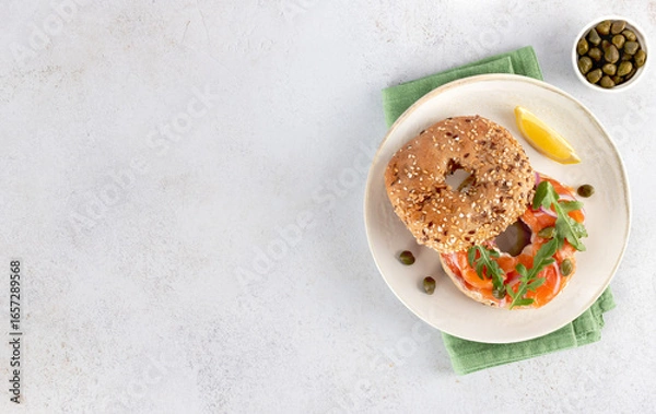 Fototapeta Bagel with salmon, cream cheese, cucumber and arugula. Top view. Copy space