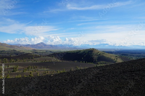 Fototapeta View over a black volcanic lava landscape from the Inferno Cone. A cinder cone rising above a landscape of black volcanic basalt rock and volcano domes from eruptions. Craters of the Moon.