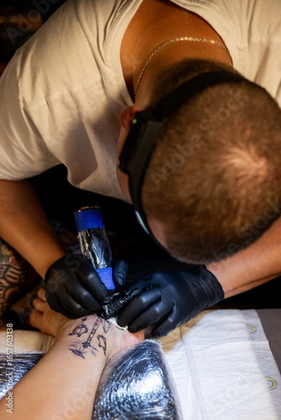 Fototapeta Tattoo artist carefully working on a client’s leg design under focused light. Concept of precision, artistry, creativity, and modern body art in a professional tattoo studio