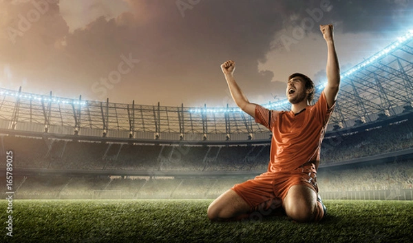 Obraz soccer player in red uniform celebrates a goal on a soccer stadium holding hands above his head and screaming