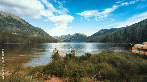 Fototapeta A peaceful lake nestled among tall mountains and lush forests, reflecting the serene blue sky and creating a harmonious, tranquil scene of natural beauty.