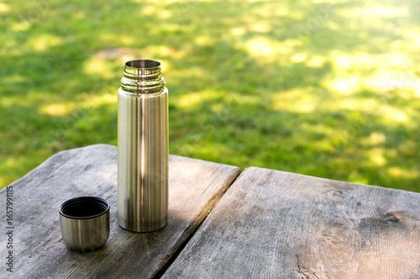 Fototapeta Coffee in a thermos on a wooden picnic table in the park. Copy space.