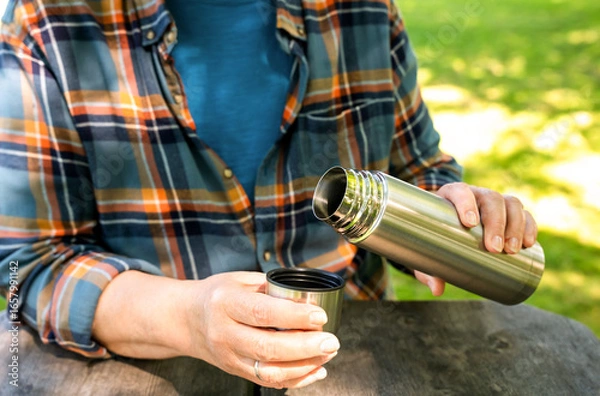 Fototapeta Elderly woman drinks coffee from a thermos on a picnic in the park. Relaxing and enjoying life. Summer or autumn sunny day. Close-up.