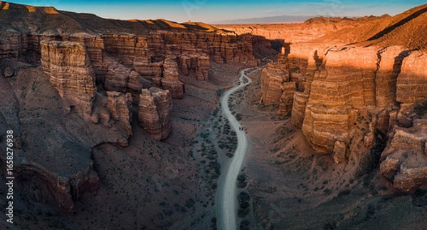 Fototapeta Winding road crossing Charyn Canyon in Kazakhstan, illuminated by the warm light of the setting sun