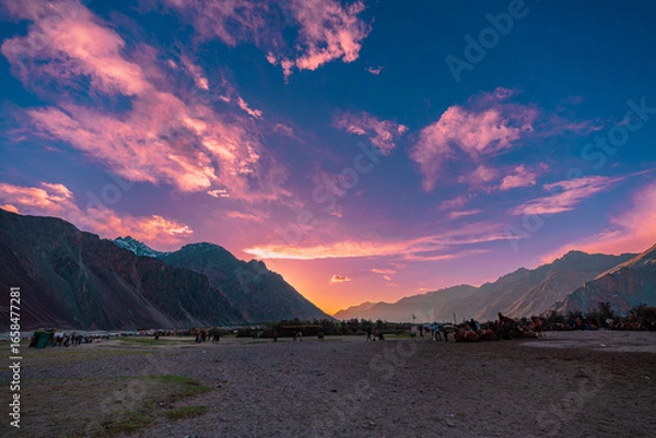 Fototapeta A breathtaking sunset across a dramatic mountain valley. The serene landscape is enriched by colorful sky. distant camel herds and towering peaks evoking a sense of peace and connection with nature.
