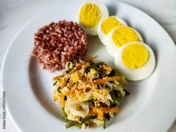Fototapeta Red rice with vegetable salad or gudangan and a boiled egg on a white plate. A healthy meal concept.