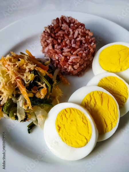 Fototapeta Red rice with vegetable salad or gudangan and a boiled egg on a white plate. A healthy meal concept.