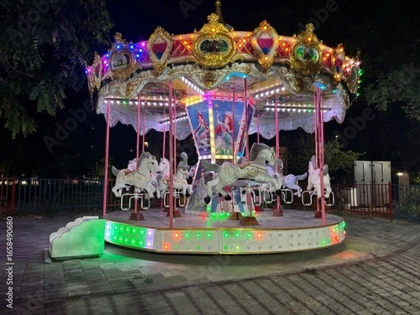 Fototapeta Carousel ride with decorative horses in an amusement park at night. Traditional fairground attraction with colorful lights and ornate details