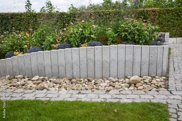 Fototapeta Modern Garden Design and Landscaping:Raised bed fenced by concrete blocks in different heights vertically erected-planted with flowers, perennial herbs-surrounded by grass, cobble and pebble stones