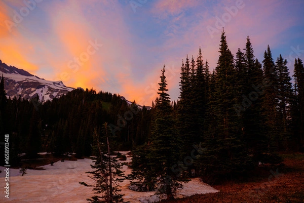 Fototapeta Stunning sunset over Mount Rainier, Washington. Vibrant sky with warm hues illuminating the rugged mountain peaks and surrounding forest.