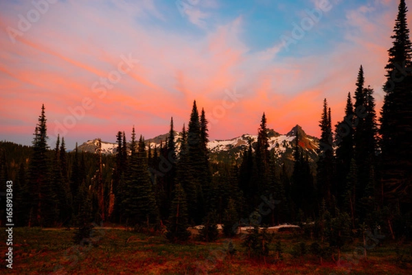 Fototapeta Stunning sunset over Mount Rainier, Washington. Vibrant sky with warm hues illuminating the rugged mountain peaks and surrounding forest.
