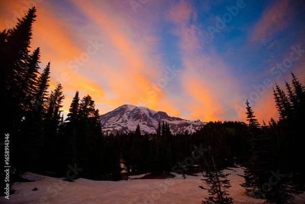 Fototapeta Stunning sunset over Mount Rainier, Washington. Vibrant sky with warm hues illuminating the rugged mountain peaks and surrounding forest.