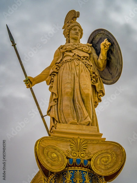 Fototapeta Statue of Athena, the Greek goddess of wisdom and knowledge, with a helmet, spear and shield on a gold gilded column. Craftsmanship highlights the power of the deity, set against a timeless backdrop.