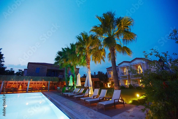 Fototapeta Evening view of cozy small Mediterranean boutique hotel pool with chaise-longue, relaxing