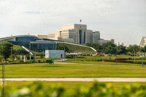 Fototapeta Modern government building in Doha, Qatar, with a green lawn in front and cloudy sky above. Contemporary architecture symbolizing state authority and progress.
