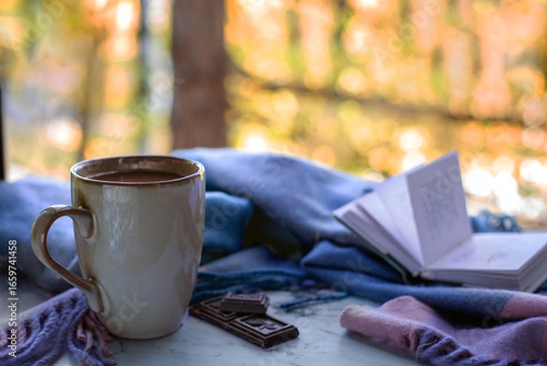 Fototapeta Tranquil autumn moment featuring warm cup of coffee, chocolate pieces, and an open book on table. For relaxation and introspection themes.