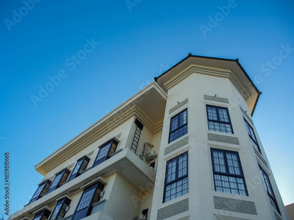 Fototapeta Exterior of building with elements of Art Deco or Mediterranean Revival architecture with clear blue sky background, low angle shot.