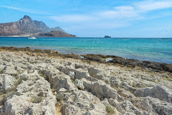 Obraz Scenic landscape of the Mediterranean sea on Crete, Greece. Rocks, lonely sailboat, mountains in the background and blue, clear sky.	  