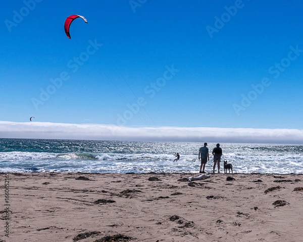 Fototapeta Lompoc, CA, USA – August 13, 2025: Bystanders watch kitesurfers take advantage of the high winds on the Pacific Ocean at Jalama Beach in Lompoc, CA.