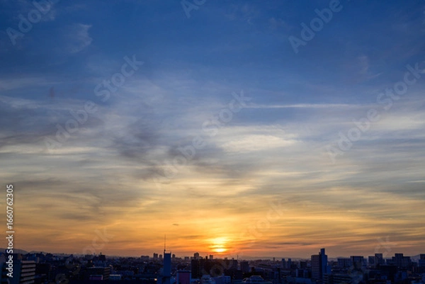 Fototapeta 神戸市の夜明け、ビルの隙間から太陽が昇り辺りはオレンジ色に染まりビルはシルエットに浮かぶ。
