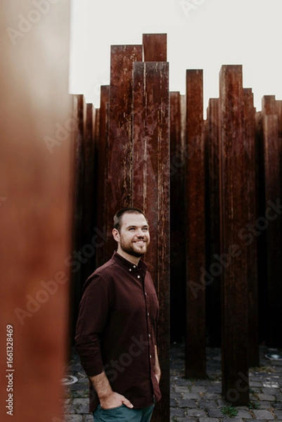 Fototapeta Smiling Man Standing Among Rusty Metal Columns