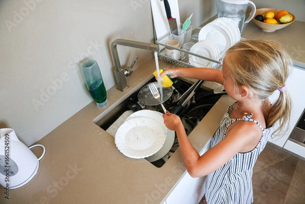 Obraz Girl cleaning fork and plate at kitchen sink with sponge